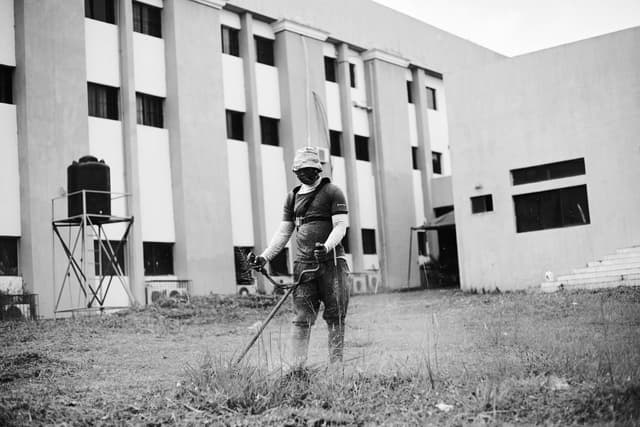 Black and white photo of a gardener using a trimmer in front of a building.