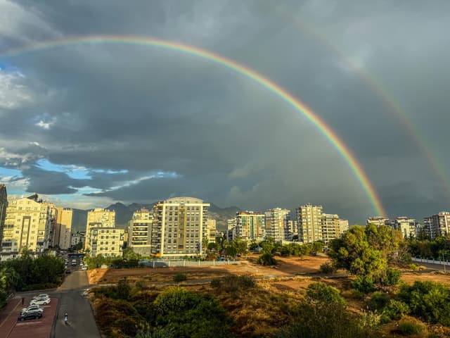 A vibrant rainbow arcs over the cityscape of Antalya, Türkiye, under dramatic skies.