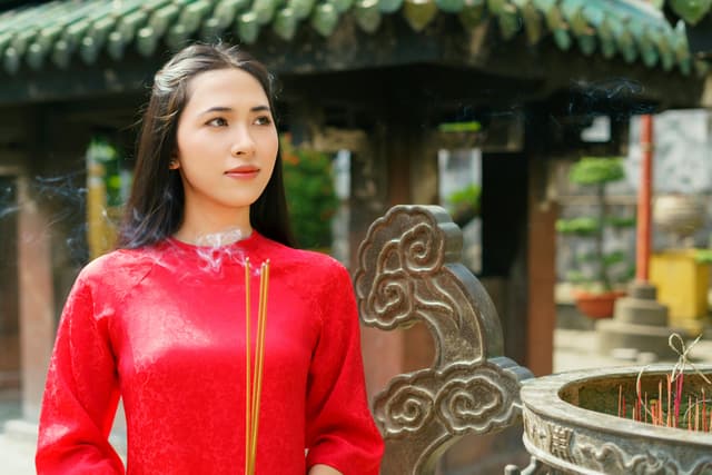 Vietnamese Woman in Traditional Attire Praying with Incense at Temple