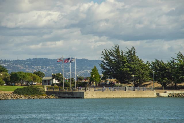 Tranquil waterfront view with waving flags and lush greenery under a cloudy sky.