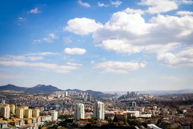 Panoramic view of Ankara with modern buildings under a bright blue sky and fluffy white clouds.