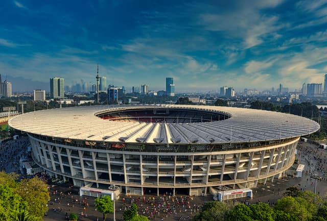 Dramatic aerial view of Gelora Bung Karno Stadium, Jakarta, surrounded by urban skyline.