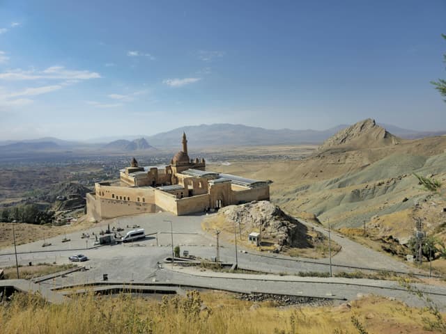 Scenic view of historic Ishak Pasha Palace amidst beautiful Ağrı landscape under clear skies.