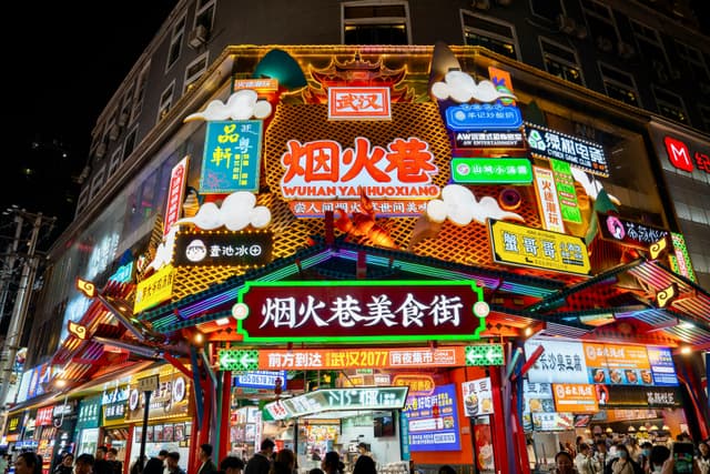 Colorful neon signs illuminate Wuhan's bustling snack street at night.