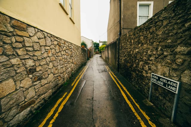 A narrow deserted alleyway in Dublin, with wet stone walls and a street sign.