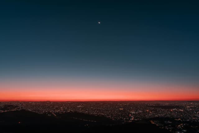 Aerial view of Belo Horizonte city lights under a crescent moon and vibrant dusk sky.