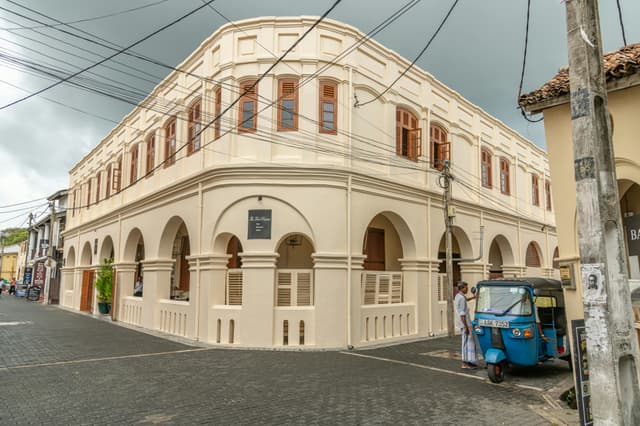 A historic colonial building in Galle, Sri Lanka with a vibrant blue tuk-tuk parked nearby.