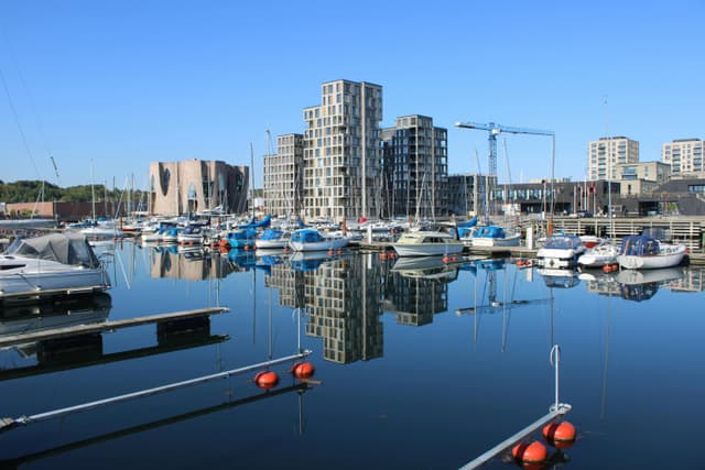 Tranquil harbor scene in Vejle, Denmark, showcasing boats, modern buildings, and a clear blue sky.