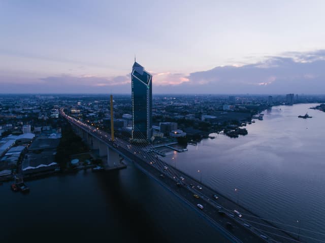 A stunning aerial view of Bangkok's Rama IX Bridge with cityscape and river at twilight.