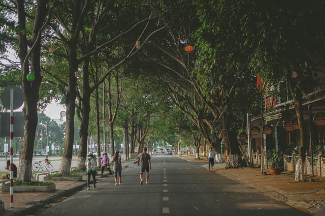 People walking along a tree-lined street in Buon Ma Thuot, capturing authentic Vietnamese urban life.
