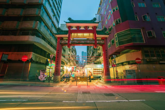 Colorful street view of Mong Kok with vibrant nightlife and traditional Chinese gate in Kowloon, Hong Kong.