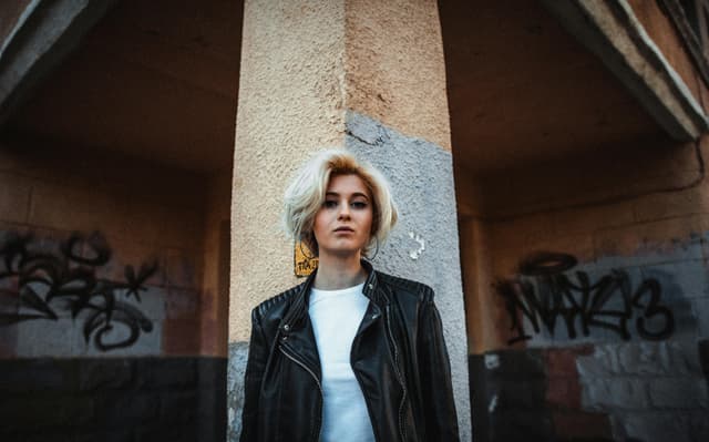 Stylish woman in leather jacket posing in urban setting with graffiti walls.
