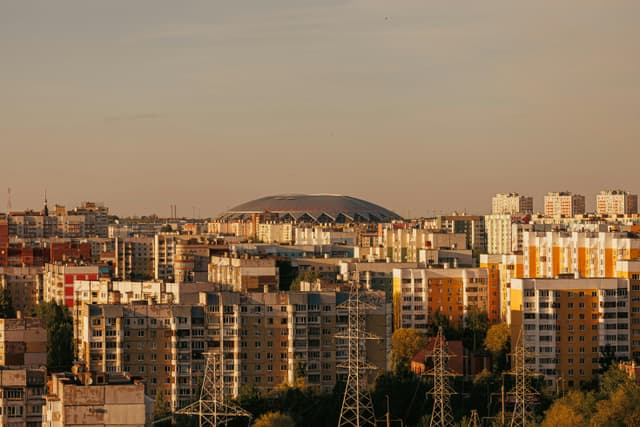 Aerial view of a cityscape with a large stadium and residential area at sunset.