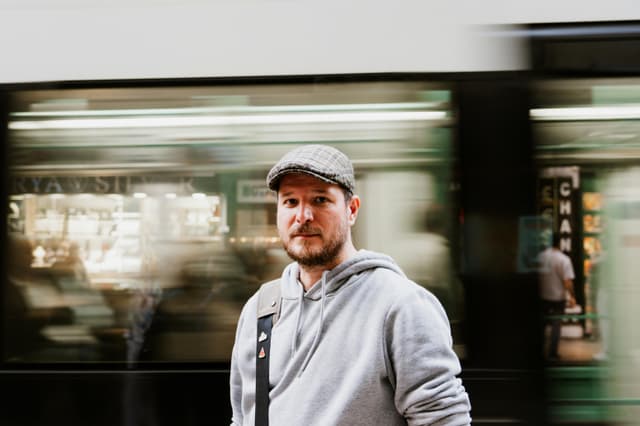 Man stands still as train blurs past in a bustling city scene.